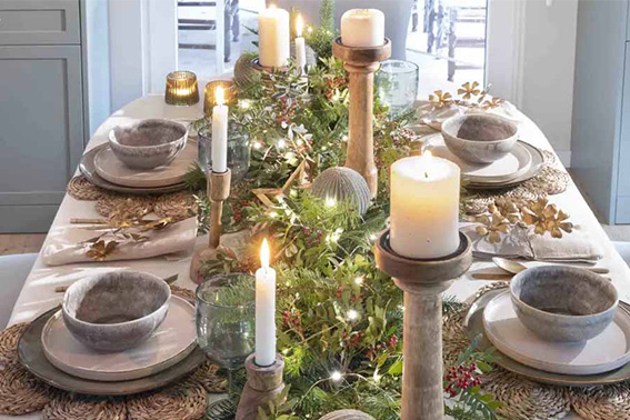 Centro de mesa navideño con velas, ramas de pino y bayas rojas sobre un mantel blanco