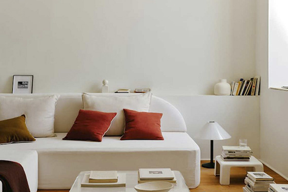 Sofá blanco con cojines y mantas en tonos cálidos, creando un ambiente acogedor y moderno.