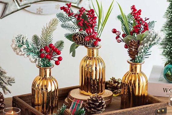 Detalles dorados para una Navidad sofisticada: centro de mesa con ramas de pino, bayas y piñas en jarrones dorados.